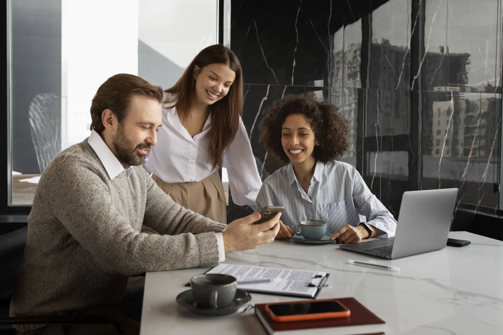 Tres colegas sonrientes revisando información en una mesa con laptop y documentos