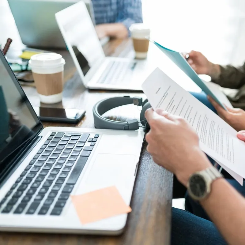 Laptop, audífonos, café y manos revisando documentos